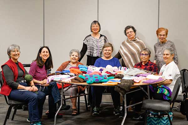 Mitzvah Knitters senior women sit around a table with their knitting projects.